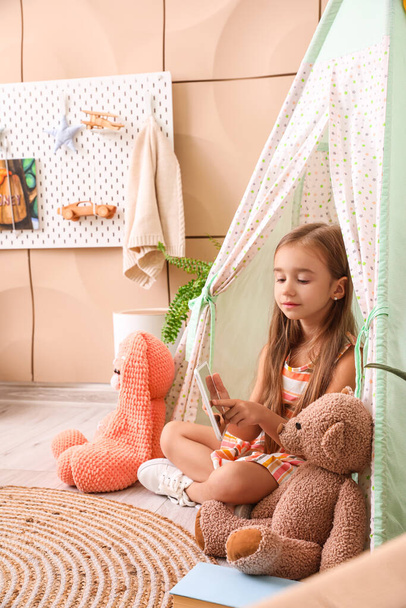 Cute little girl z zabawkami za pomocą tabletu w namiocie zabaw w domu - Zdjęcie, obraz