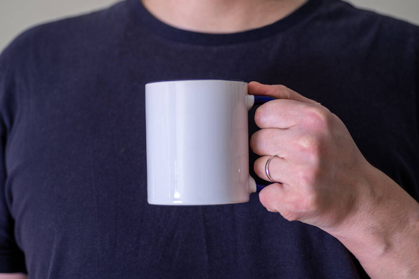 Man holding a white cup of hot beverage outdoors. Man's hand holding a blank mug against black background. Close up, mockup image, copy space for text. - Fotó, kép