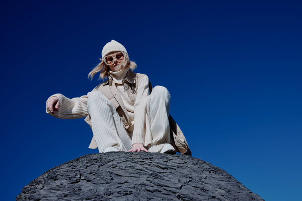 νεαρή γυναίκα κάθεται σε ένα πέτρινο γαλάζιο ουρανό σε έναν τρόπο ζωής καπέλο - Φωτογραφία, εικόνα