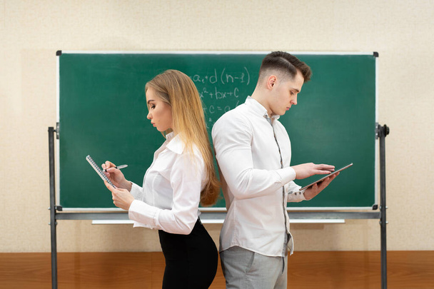 University students a guy and a girl pose with tablets in their hands near the blackboard - Fotoğraf, Görsel