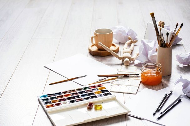Watercolour, stack of paper, paintbrushes and other artistic equipment on floor at home. Home tutoring, education, DIY, hobby or leisure concept.  - Foto, imagen