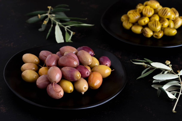 Olive marinate miste (verdi e viola) su fondo scuro. Olive di colore saporito nel piatto. Olive grigliate sullo sfondo - Foto, immagini