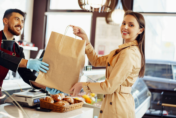 Помічник магазину обробляє сумку для покупки жінки-клієнта в продуктовому магазині
 - Фото, зображення