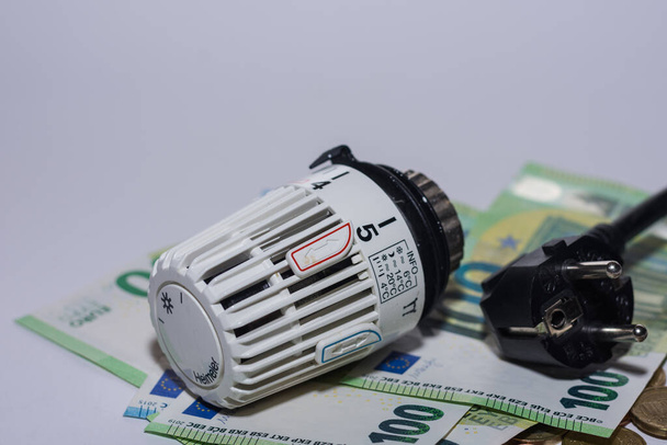 Aumento de los precios de la energía y consumo de energía termostático controlador de calefacción y enchufe de electricidad y billetes de 100 euros con fondo gris - Foto, imagen