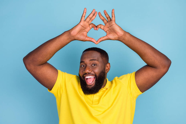 Photo of funny impressed dark skin guy dressed yellow t-shirt showing hands arms heart smiling isolated blue color background - Fotografie, Obrázek