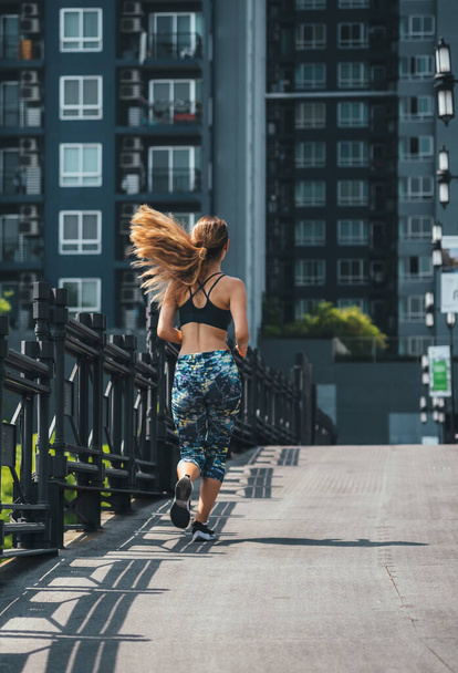 Rückansicht einer Frau, die in der Stadt läuft. Rückenansicht einer nicht wiedererkennbaren Sportlerin beim Joggen im Freien. - Foto, Bild
