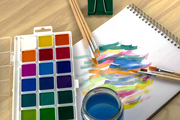 watercolor paints a jar of water a stationery clip and brushes on a white sheet with flower samples. High quality photo - Photo, Image