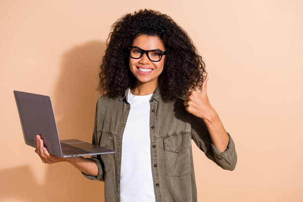 Portrait of attractive trendy cheerful skilled girl showing thumbup using laptop isolated over beige pastel color background - Φωτογραφία, εικόνα