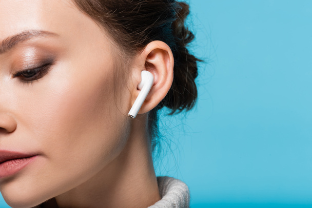 Cropped view of young woman in earphone isolated on blue - 写真・画像