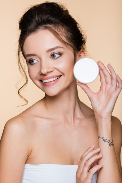 Cheerful model holding container with cosmetic cream isolated on beige  - Foto, immagini