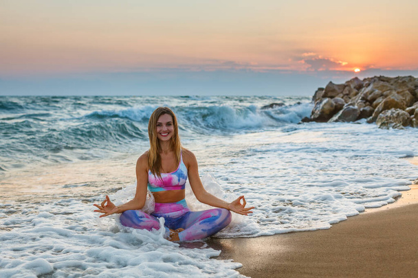Beautiful woman practicing yoga sitting in a lotus position on the beach during sunset. Inner harmony and self body care. - Fotoğraf, Görsel