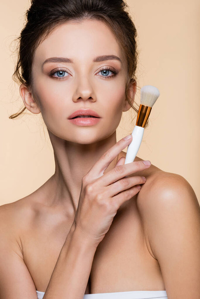 Pretty brunette model holding cosmetic brush while posing isolated on beige  - Photo, Image