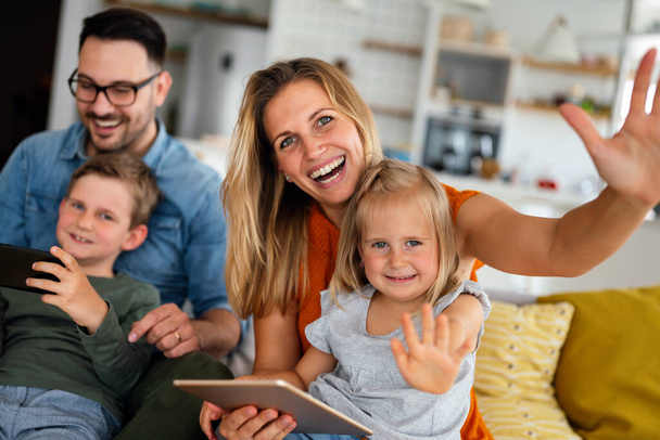 Счастливая молодая семья, весело проводящая время дома. Родители с детьми с помощью цифрового устройства. Концепция счастливого воспитания. - Фото, изображение