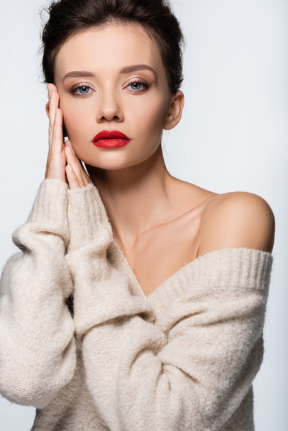 Trendy model in sweater touching face and looking at camera isolated on white - Photo, image