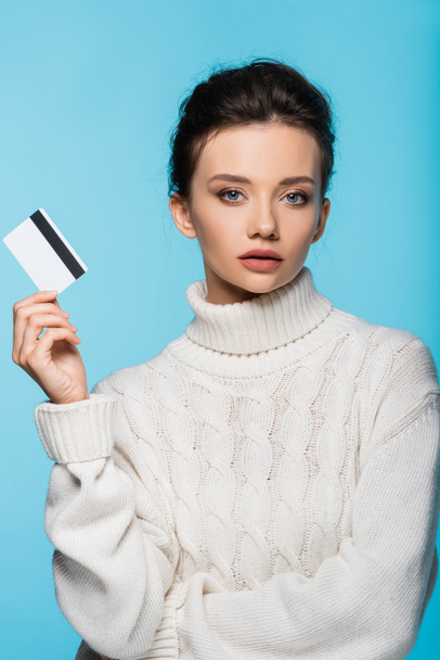 Pretty model in knitted sweater holding credit card isolated on blue - Foto, afbeelding