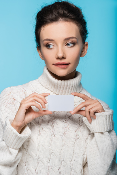 Pensive woman in sweater holding blank card isolated on blue - Foto, Imagen