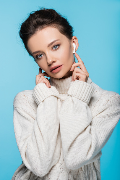 Pretty woman in earphone and sweater looking at camera isolated on blue - Fotó, kép