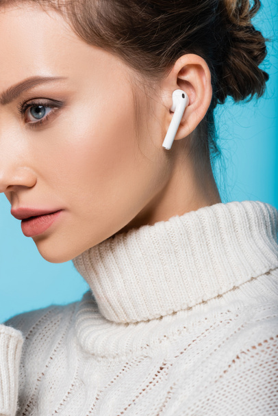 Cropped view of woman in knitted sweater and wireless earphone isolated on blue - Foto, Imagen
