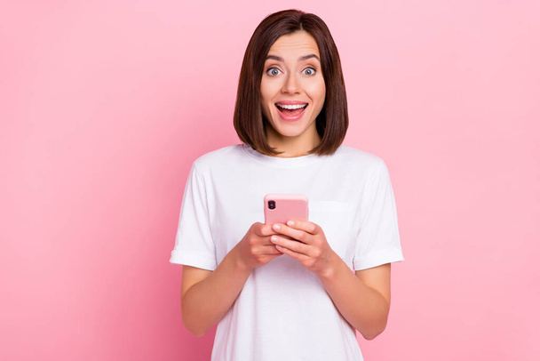 Photo of young amazed female communicating on smartphone hear good news isolated on pink color background - Foto, afbeelding