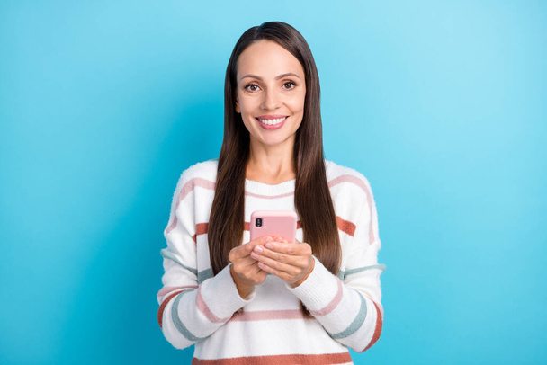 Zdjęcie wesołej pani trzymać telefon aplikacji powiadomienia przedłożyć nosić paski sweter odizolowany niebieski kolor tła - Zdjęcie, obraz