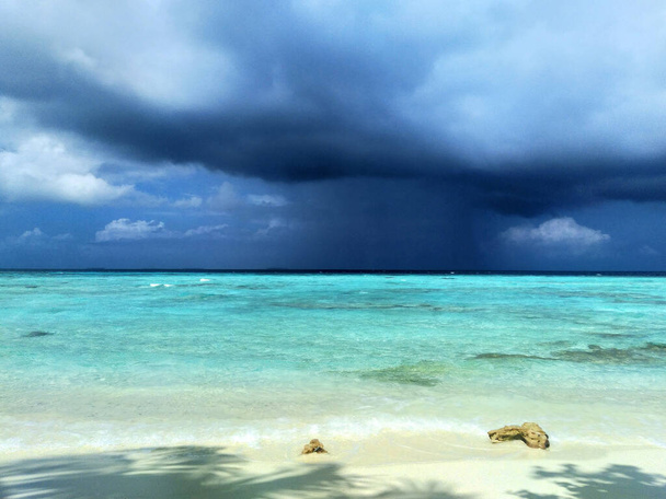 A sky with dark storm clouds. A rain over a calm sea. Maldives, a beach with the white sand near the turquoise ocean. - Foto, Bild