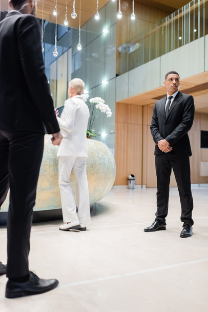 homens de segurança interracial em pé perto de empresária sênior check-in na recepção do hotel - Foto, Imagem