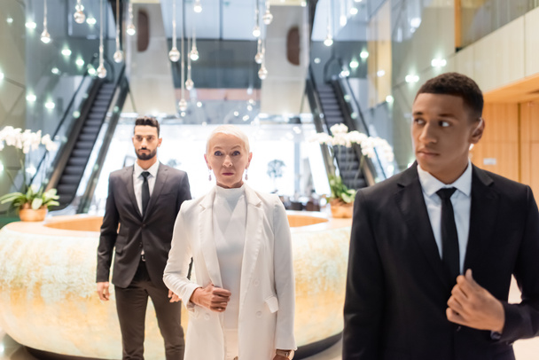 interracial security men escorting senior businesswoman in modern hotel - Foto, imagen