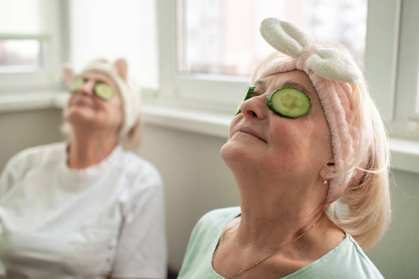 Two happy senior women apply facial cosmetic mask, have fun at home, body positivity, ageism - Photo, Image