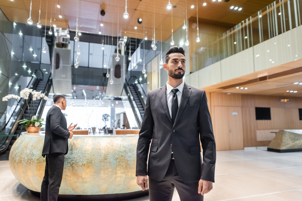 uomo di sicurezza bi-razziale in giacca e cravatta in piedi nella hall dell'hotel vicino alla guardia afroamericana alla reception - Foto, immagini