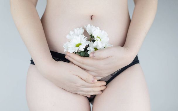 Close-up of a woman body. Female pubis. Panties from which flowers stick out. Concept photo about feminine intimate health. Delicate and sensual frame without a hint of eroticism. Selective focus. - Photo, Image