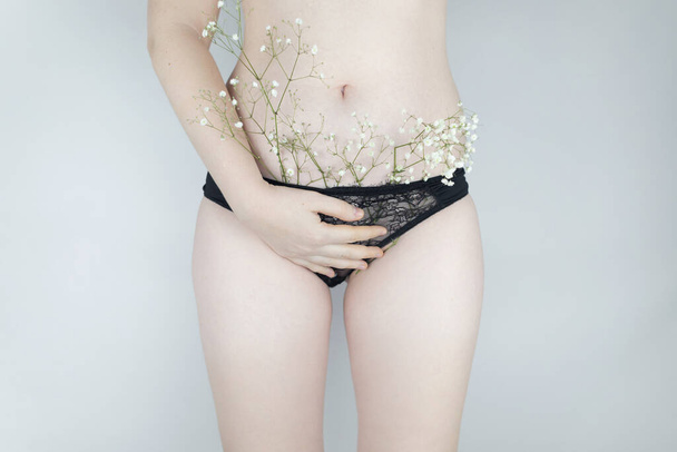 Een vrouw heeft kleine bloemen die onder haar onderbroek vandaan steken, die extra haar imiteren. Laserontharing en scheren met een scheermes. Conceptueel schot over vrouwenkwesties. Juiste zelfzorg. - Foto, afbeelding