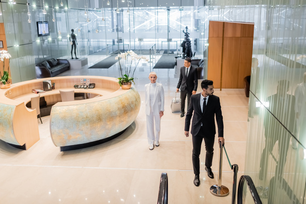 high angle view of multiethnic bodyguards in formal wear escorting senior business lady in luxury hotel - Photo, Image