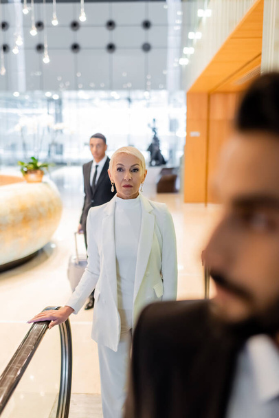 selective focus of trendy senior businesswoman near blurred multiethnic bodyguards in hotel - Foto, Imagem