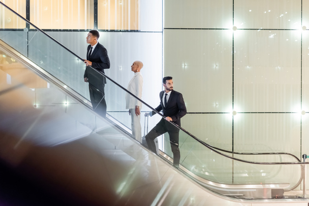 mature businesswoman on hotel escalator near interracial bodyguards - Photo, image