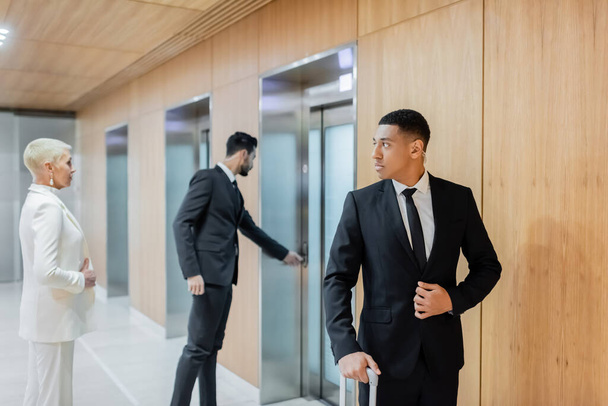 interracial bodyguards escorting senior businesswoman near elevators in hotel - Photo, Image