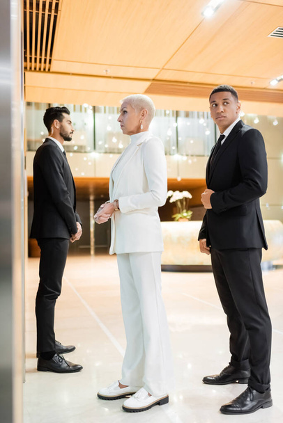 Вид богатой бизнесвумен в полный рост рядом с частными телохранителями в отеле - Фото, изображение