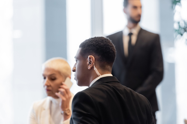 Αφροαμερικανός σωματοφύλακας κοντά σε ώριμη επιχειρηματίας μιλώντας στο smartphone του ξενοδοχείου - Φωτογραφία, εικόνα