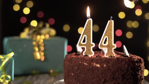 Negyvennégy szülinapi gyertya egy édes tortán az asztalon, 44. születésnap. Tűz az öngyújtóból, fújd el az ünnepi gyertyát.. - Felvétel, videó