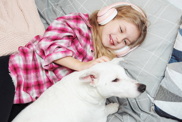 Girl and dog laying on couch in headphones, listening to music with her smarthphone. - Foto, Imagen
