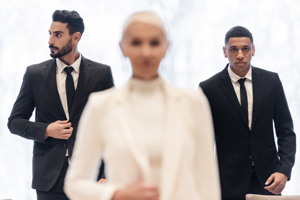 interracial bodyguards in formal wear escorting blurred businesswoman during business trip - Фото, зображення