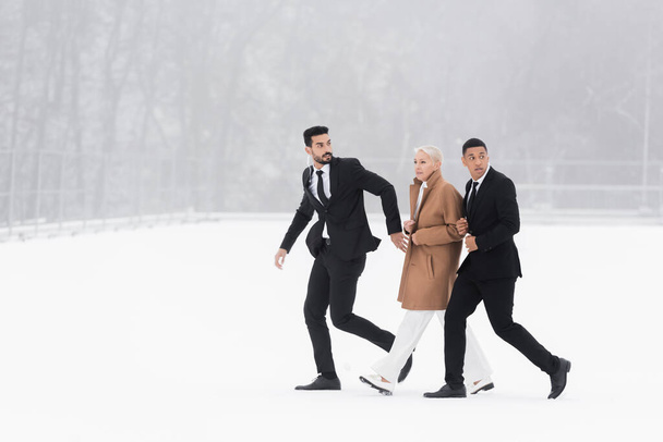 pełny widok długości wieloetnicznych ochroniarzy chroniących dojrzałą businesswoman chodzenie po polu zimowym - Zdjęcie, obraz