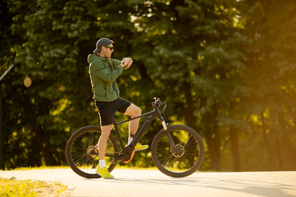 Handsome young man checking time ebike in nature - Foto, Imagen