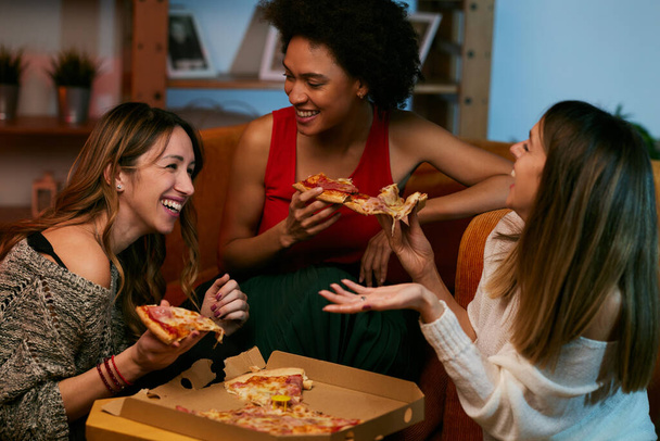 Szczęśliwy wielokulturowe kobiety przyjaciele posiadające imprezę w domu i jedzenia pizzy. - Zdjęcie, obraz