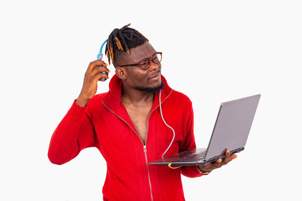 młody student z plecionymi włosami stojący na białym tle usuwający słuchawki trzymając laptopa. - Zdjęcie, obraz
