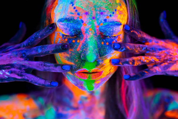 Beautiful young woman in neon light. Portrait of a model with fluorescent makeup posing in UV light with colorful makeup. - Valokuva, kuva