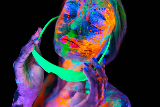 Beautiful model woman wearing glasses with colorful bright fluorescent makeup in neon light, nightclub disco - Foto, afbeelding