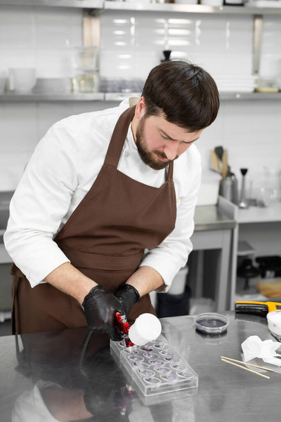 Male pastry chef holds chocolate candy molds and sprays food paint with a pastry airbrush in the kitchen - Foto, immagini
