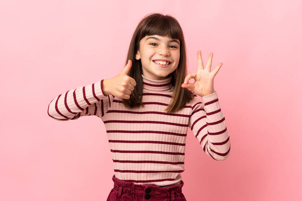 Menina isolada no fundo rosa mostrando sinal ok e polegar para cima gesto - Foto, Imagem