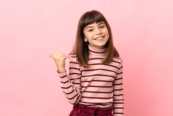Little girl isolated on pink background pointing to the side to present a product - Photo, Image