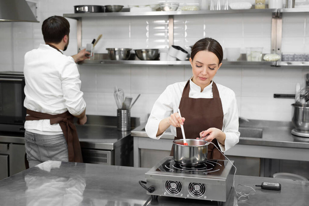 Man and woman confectioners prepare dessert together in a professional kitchen - Foto, Bild
